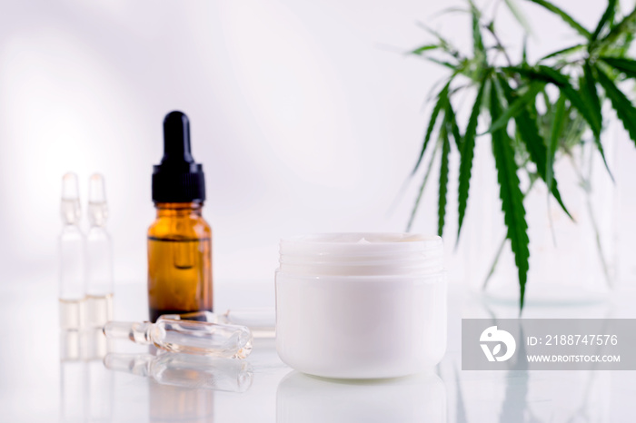 Natural cosmetics with cannabis oil. Mockup with a White clean jar with cosmetics cream and green leaves of hemp.