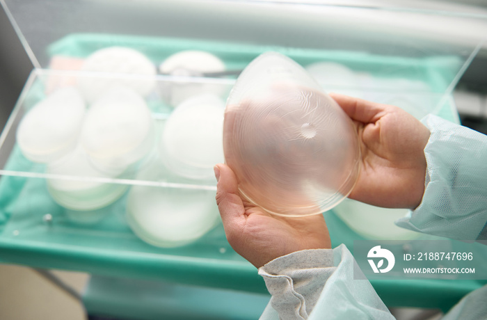 Breast silicone implant in surgeon hands on the background of medical samples of breast prosthesis of various sizes for aesthetic plastic surgery after resection due to breast cancer disease.