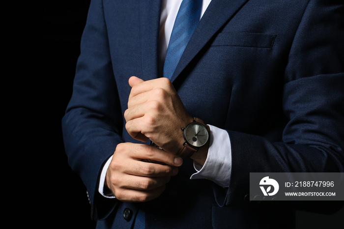 Young businessman with stylish wristwatch on dark background