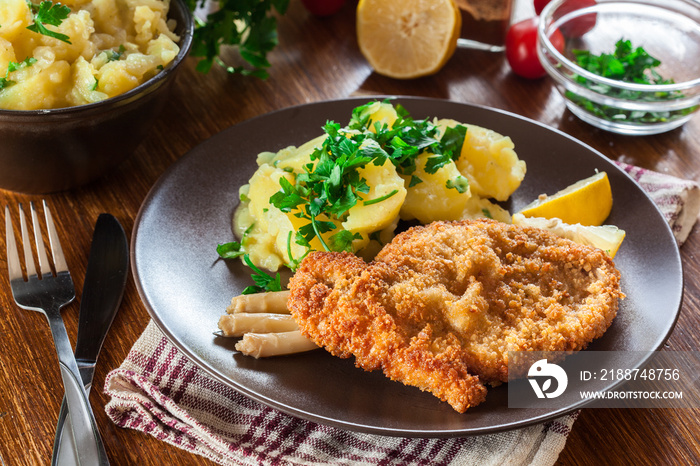 Homemade breaded viennese schnitzel with potato salad and asparagus on a plate