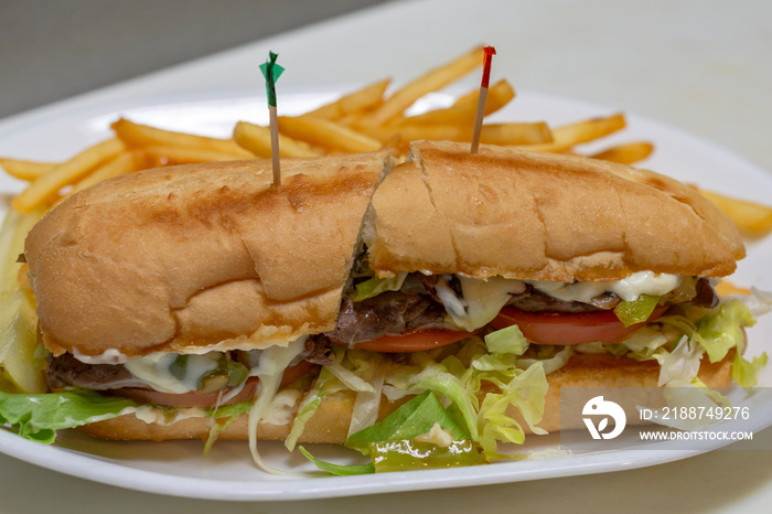 Philadelphia cheesesteak sandwich on a sub bun.  White platter with toothpicks.  Halved.  French fries in background.