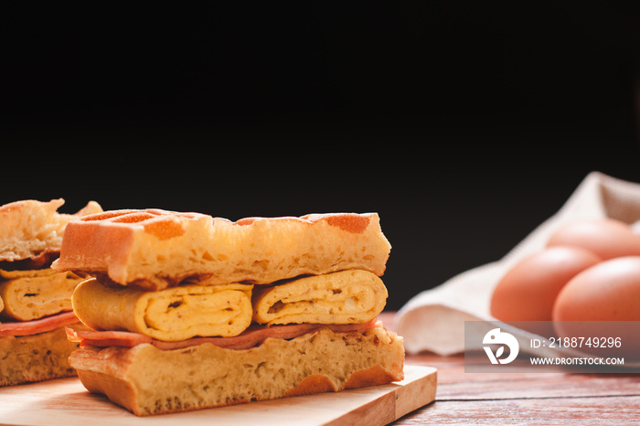 Waffle sandwich with egg and chicken ham on chopping board on wooden table and black background. Homemade food concept.