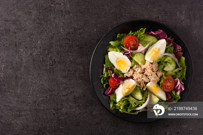 Salad with tuna, egg and vegetables on black background top view copy space