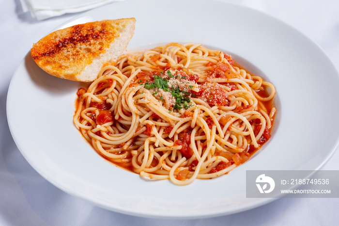 A view of a plate of spaghetti and marinara sauce, with a piece of garlic bread, in a restaurant or kitchen setting.