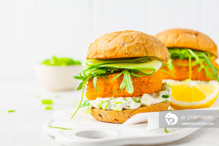 Fish burger with cucumber, arugula and mayonnaise sauce, white background.