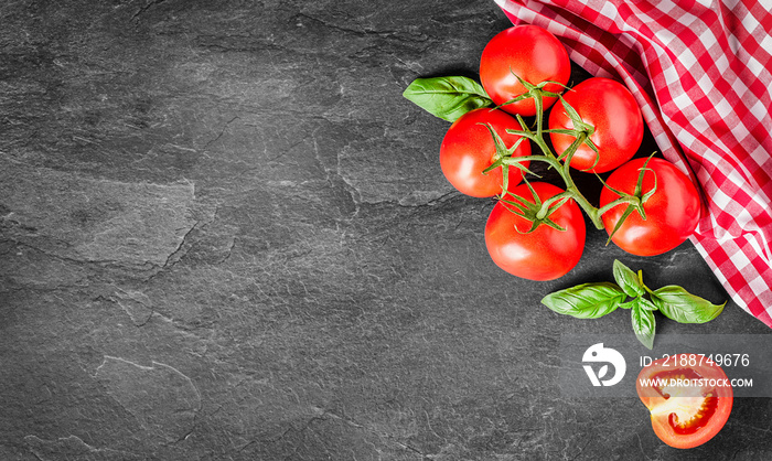 Fresh tomatoes on black background top view banner or copy space. Ript red tomato vegetables with basil leaves on dark stone table with red white cubes cloth in right corner.