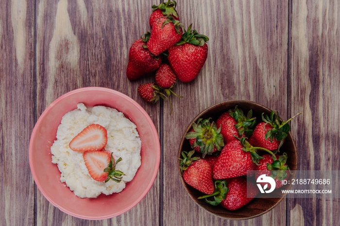 top view of cottage cheese in a pink bowl with fresh ripe strawberries on rustic wooden background