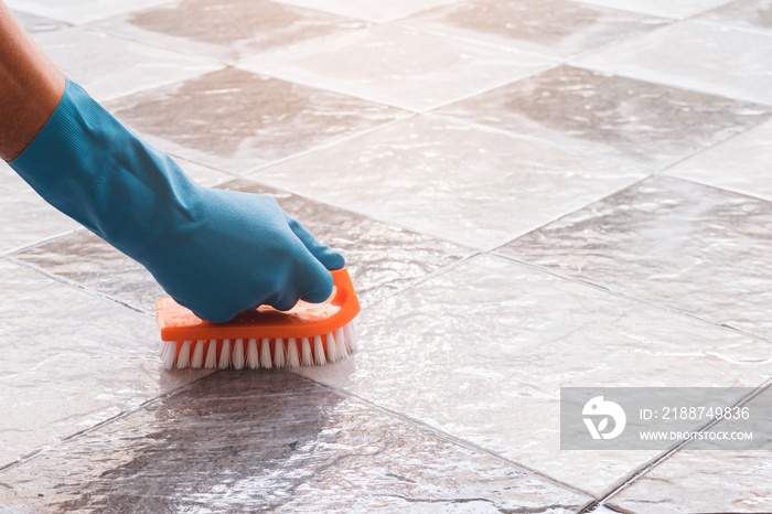 Hand of man wearing blue rubber gloves is used to convert scrub cleaning on the tile floor.