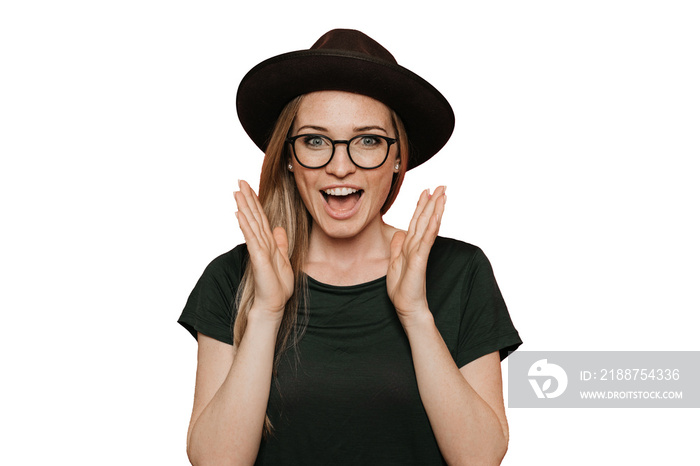 Excited redhead young woman in glasses, casual green t-shirt and hat with brim, screams happily, raises her hands up in surprise, over transparent background with copy space. Sincere people emotions.