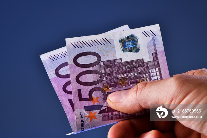 A man hand shows 1000 Euros in two 500 euro banknotes on a blue background