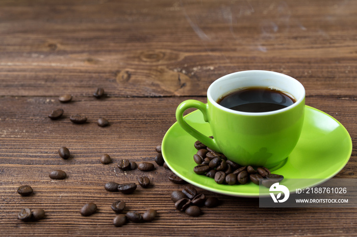 Green cup of hot coffee and coffee beans on wooden table