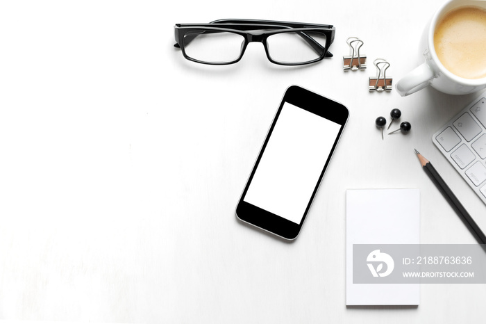 on a white table background from above smartphone, eye glasses, coffee cup pen and paper isolated