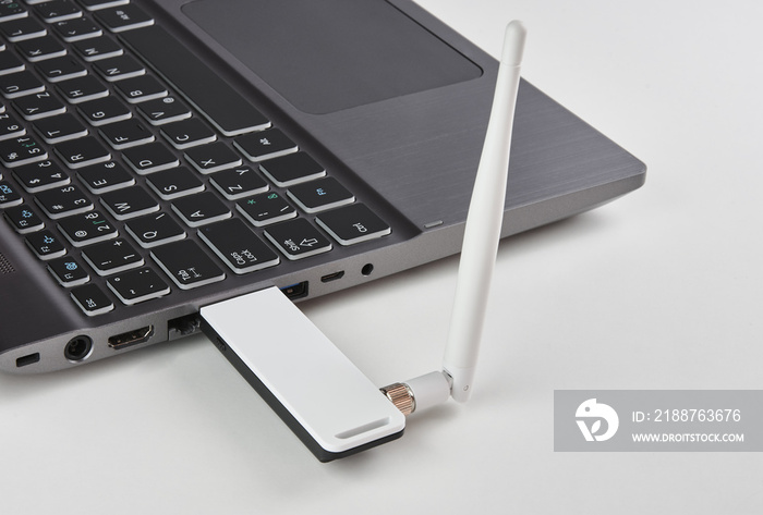 Silver laptop with USB modem plugged in with an antenna, on a white table