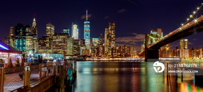 New York City Brooklyn Bridge and Manhattan skyline with skyscrapers over Hudson River illuminated  lights at dusk after sunset.