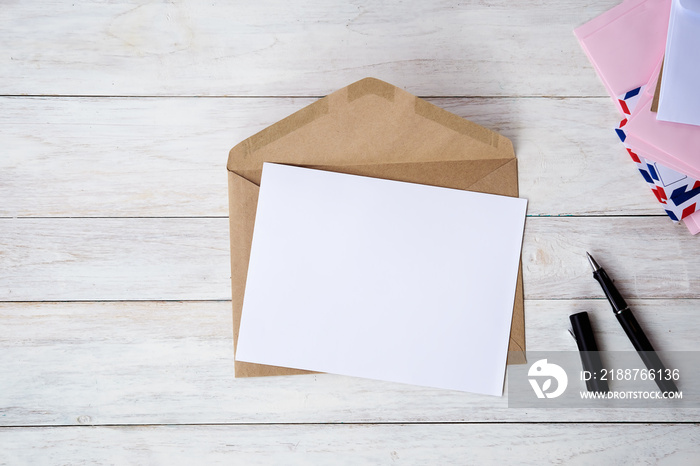 Top view of envelope and blank greeting card with rose flowers on white wooden background.