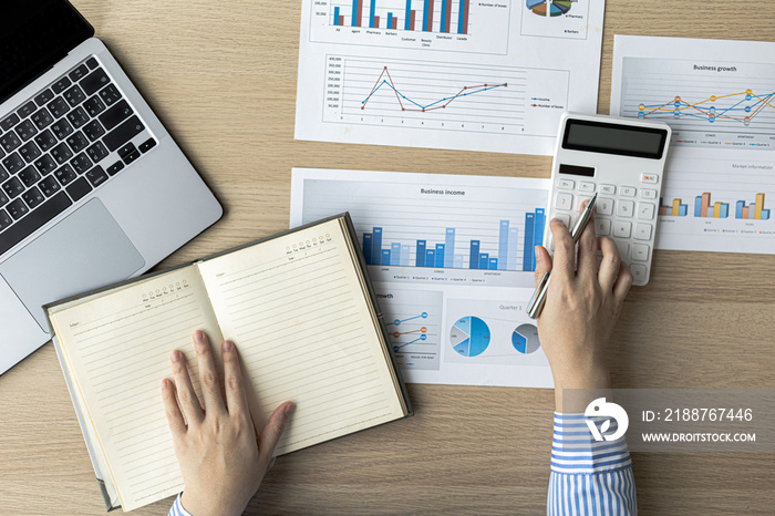 A businesswoman presses on a white calculator and looks at the numbers from a notebook she notes during a finance department meeting to check the accuracy of the numbers on the report. Finance concept