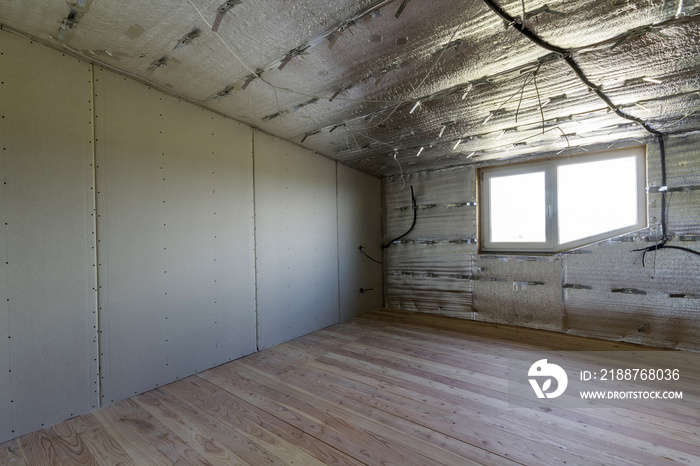 Room under construction with silver aluminum insulation foil and drywall on walls and ceiling.