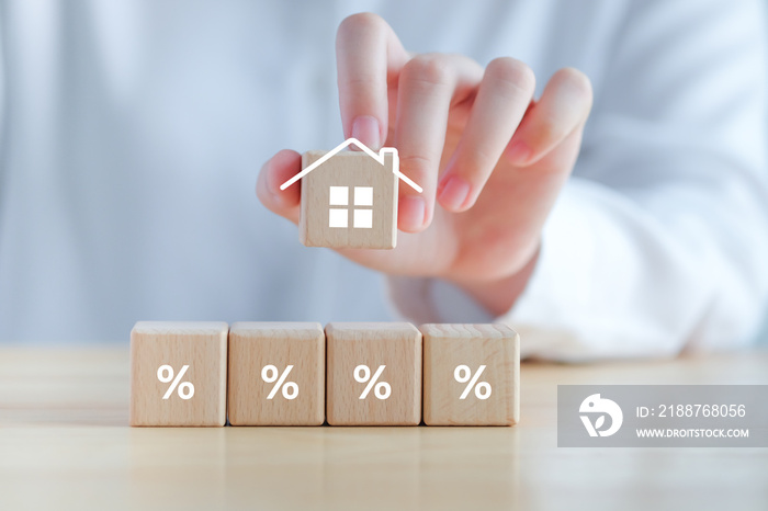 Hand holding house icon with Percentage sign on wooden block. Refinance to reduce the interest of home loan. Mortgage, loan, repayments, credit limit, house tax, business and financial concept.