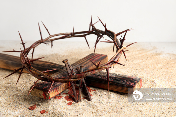 Crown of thorns with wooden cross, nails and blood drops on sand