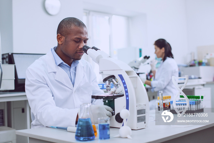 We are professionals. Inspired professional biologist working with his microscope and his co-worker working in the background