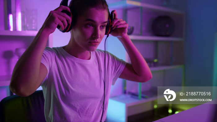 Closeup focused gamer putting headphones at home room. Cyberspace neon interior