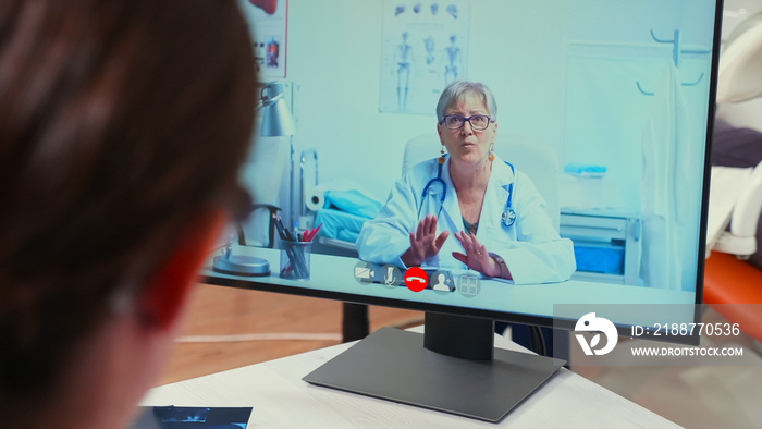 Back view of nurse discussing on webcam with senior specialist stomatologist using mobile phone sitting in dental clinic in front of pc with digital x-ray. Dentistry doctor explaining patient symptoms