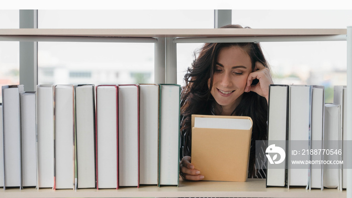 caucasian woman at book shelf in library searching and reading book