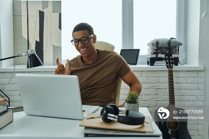 Cheerful young African man gesturing while having web conference in office