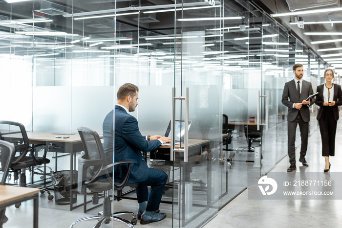 Business people walking in the hallway of the modern office building with employees working behind glass partitions. Work in a large business corporation