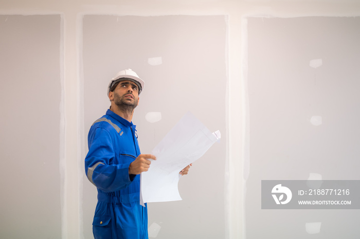 Arab civil engineer wearing safety uniforms workwear  Standing holding a blueprint of a real estate construction project to check the construction progress at the construction site.