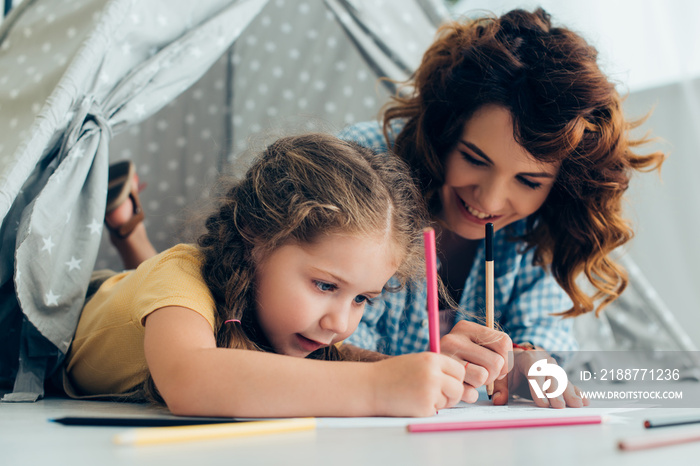 Happy babysitter and child drawing together in play tent