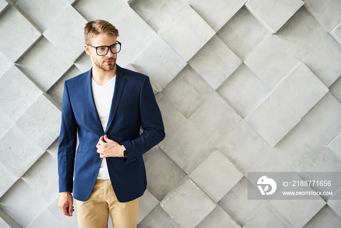 Waist up portrait of male standing and touching jacket. He is wearing eyeglasses and looking sideways confidently. Copy space in right side