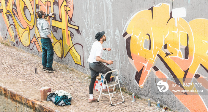 Graffiti artists friends painting with color spray on the wall for international competition - Focus on right guy face