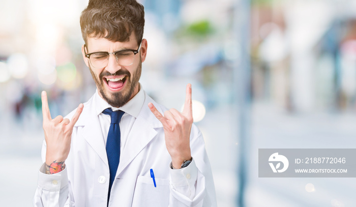 Young professional scientist man wearing white coat over isolated background shouting with crazy expression doing rock symbol with hands up. Music star. Heavy concept.