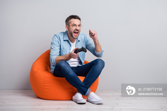 Portrait of his he nice attractive cheerful cheery overjoyed gray-haired guy sitting in bag chair playing game having fun spending free time isolated over gray light pastel color background