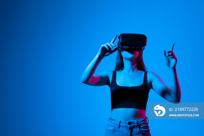 Young brunette woman wearing virtual reality device, vr glasses and playing a game with a friends online in neon light.