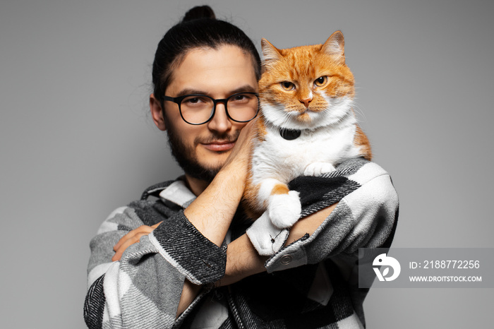 Studio portrait of young man with red cat on his shoulder. Grey background.