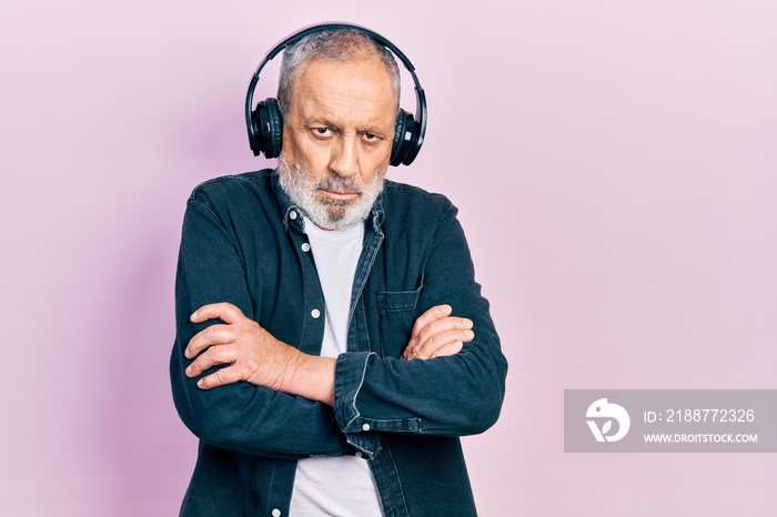 Handsome senior man with beard listening to music using headphones skeptic and nervous, disapproving expression on face with crossed arms. negative person.