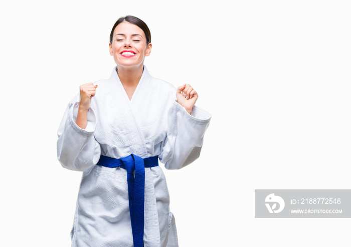 Young beautiful woman wearing karate kimono uniform over isolated background excited for success with arms raised celebrating victory smiling. Winner concept.
