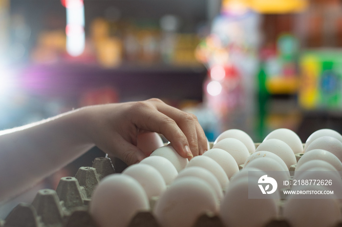 hand of a woman taking some white chicken eggs, girl selling eggs in a grocery store. eggs rich in protein albumen ready to be sold and consumed in different foods. food concept