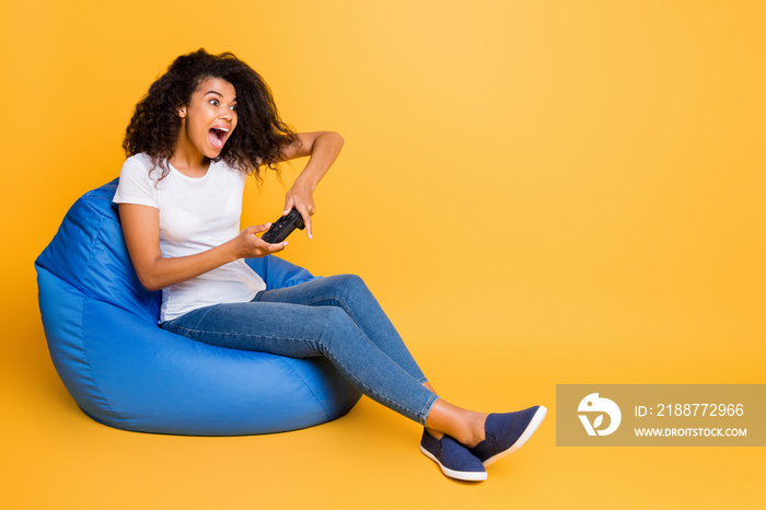 Portrait of nice attractive lovely cheerful cheery glad wavy-haired girl sitting in bag chair playing video game having fun isolated over bright vivid shine vibrant yellow color background