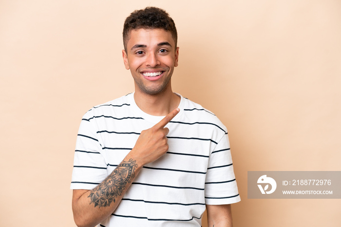 Young Brazilian man isolated on beige background pointing to the side to present a product