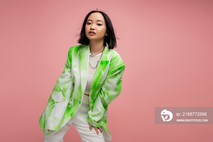 young asian woman in trendy green and white jacket looking at camera while posing isolated on pink.