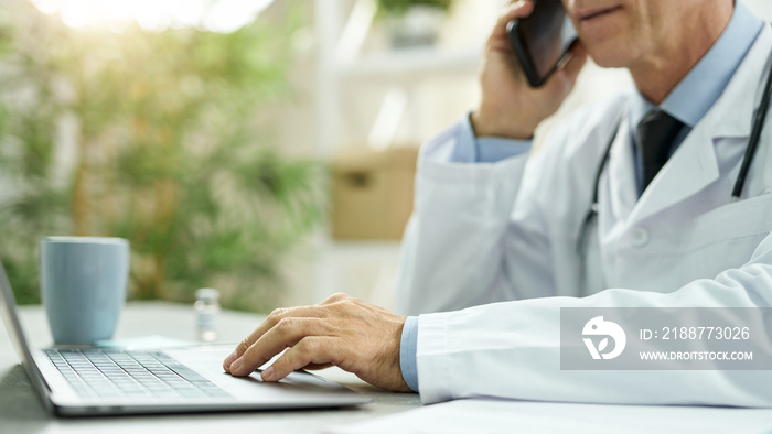 Doctor talking on mobile phone and using laptop at work