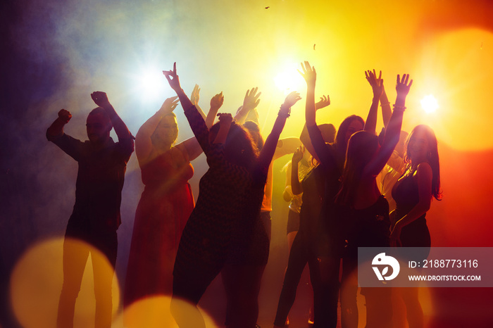 Friendship. A crowd of people in silhouette raises their hands on dancefloor on neon light background. Night life, club, music, dance, motion, youth. Yellow-blue colors and moving girls and boys.