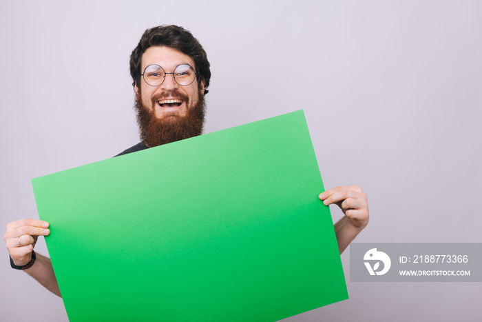 Portrait of smiling bearded man holding blank banner in hands isolated on gray background