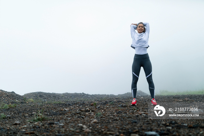 Athletic woman stretching while warming up in nature on foggy day,