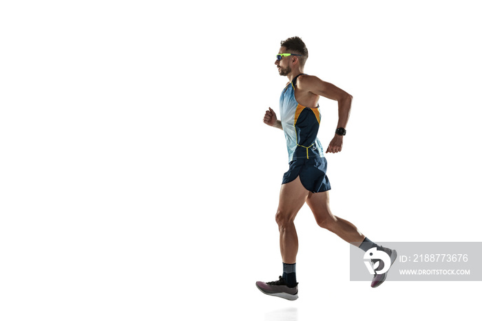 Triathlon male athlete running isolated on white studio background. Caucasian fit jogger, triathlete training wearing sports equipment. Concept of healthy lifestyle, sport, action, motion. Side view.