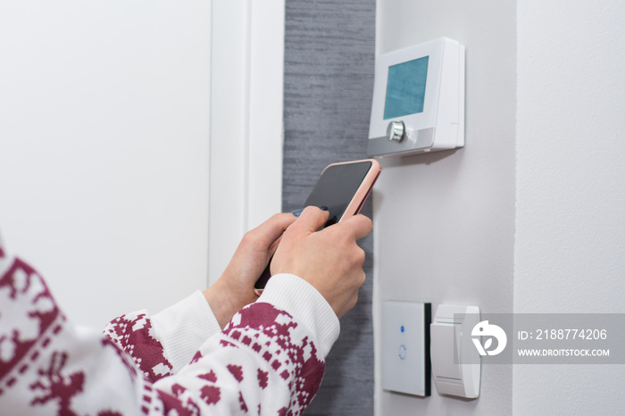 Girl adjusts and regulate the room temperature with smart phone on switch wall. Smart WiFi light switch and temperature regulator. Smart house concept. Close up, selective focus
