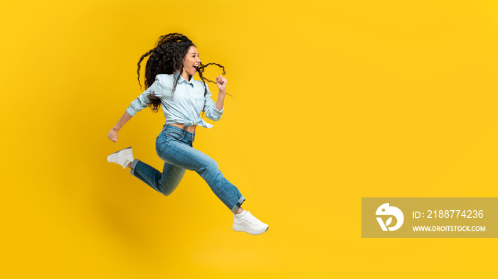 Excited young woman jumping up at orange studio